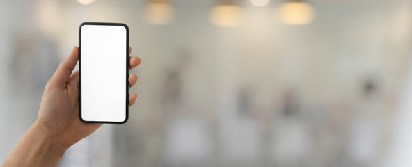 Cropped shot of a man holding blank screen smartphone in blurred glass wall office