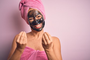 Wall Mural - Middle age brunette woman wearing beauty black face mask over isolated pink background doing money gesture with hands, asking for salary payment, millionaire business