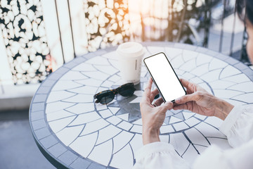 Mockup image blank white screen cell phone.woman hand holding texting using mobile on desk at coffee shop.background empty space for advertise text.people contact marketing business,technology