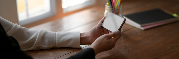  Cropped shot of female freelancer holding horizontal blank screen smartphone on wooden table