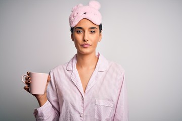 Wall Mural - Young beautiful brunette woman wearing pajama and sleep mask drinking cup of coffee with a confident expression on smart face thinking serious