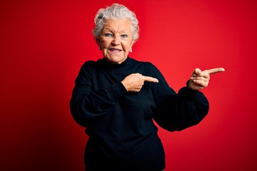 Senior beautiful woman wearing casual sweater standing over isolated red background smiling and looking at the camera pointing with two hands and fingers to the side.