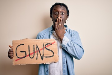 Canvas Print - Young african american man asking for peace holding banner with prohibited guns message cover mouth with hand shocked with shame for mistake, expression of fear, scared in silence, secret concept