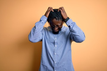 Canvas Print - Young handsome african american man wearing shirt and glasses over yellow background suffering from headache desperate and stressed because pain and migraine. Hands on head.