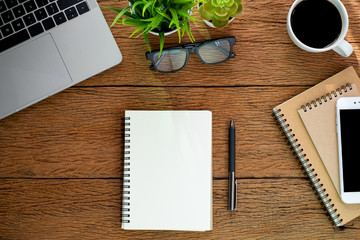 Top view from above of Blank notebook with laptop, glasses and coffee on wood table background. Workplace for creative work of designer at home. Flat lay, Business-finance concept with copy space.