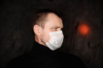 Wall Mural - Photo Caucasian man in a medical mask with a red light on a black background