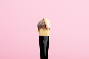 Makeup brush with drop of face foundation. Daily facial treatment. Equipment for cosmetology products. Professional cosmetics and wellness concept. Isolated on pink backdrop