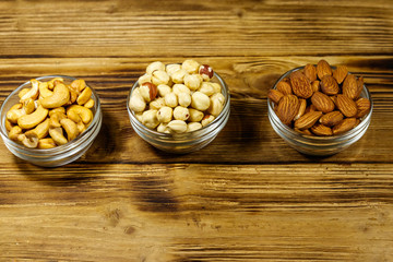 Sticker - Assortment of nuts on wooden table. Almond, hazelnut and cashew in glass bowls. Healthy eating concept