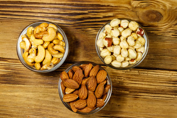 Sticker - Assortment of nuts on wooden table. Almond, hazelnut and cashew in glass bowls. Top view. Healthy eating concept