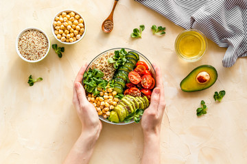 Wall Mural - Quinoa, avocado and chickpeas in bowl in hands - balanced healthy food - on beige table. Top view