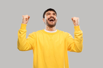 Sticker - success, emotion and expression concept - happy man in yellow sweatshirt celebrating victory over grey background