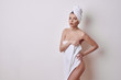 Alluring young naked woman covering her breasts and front of her torso with a fresh clean white a towel as she looks at camera with a sultry expression and parted lips over a white studio background