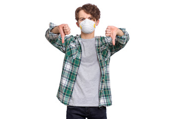 Poster - Concept of coronavirus quarantine. COVID-19. Teenager wearing medical protective face mask to health protection from influenza virus, isolated on white background. Teen boy giving thumb down gesture.