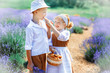 Village scene with children in vintage clothes in middle of lavender field. Girl in brown dress with white apron feed boy in white hat, shirt and brown trousers. Picnic in lavender. Eating outdoor