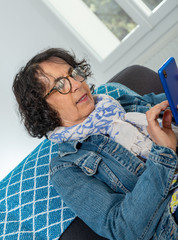 Wall Mural - cheerful brunette senior woman using smartphone while sitting on sofa