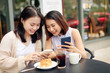 © makistock - Two young women having coffee break together use smart phone. Happy women using cell phone at sidewalk cafe