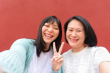 Wall Mural - Asian mother and daughter taking selfie with mobile smartphone outdoor - Happy Chinese family having fun sharing online photos for social media - People parents and technology lifestyle concept