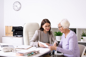 Wall Mural - Senior female client looking at insurance form and listening to young agent