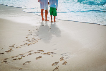 mother and son walking on beach leaving footprint in sand