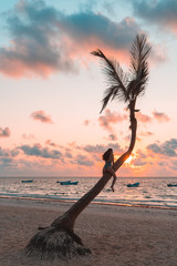 Girl sitting on a palm tree at sunrise on the sandy beach of the Caribbean i