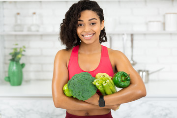 Wall Mural - Happy young african girl holding green vegetables