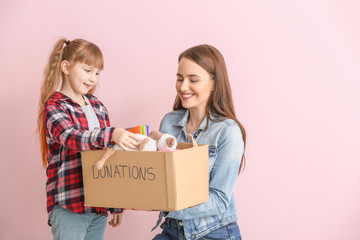 Wall Mural - Volunteer with donations for orphans and little girl on color background