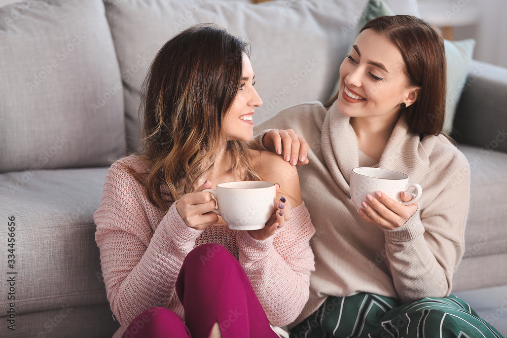Young women in warm sweaters drinking tea at home