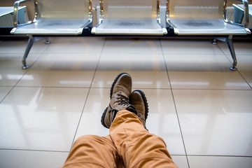 man sitting with his legs in hiking boots on floor in the airport parking lot waiting for his connec