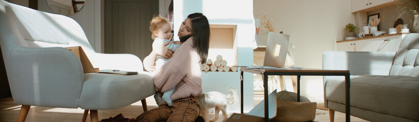 Wall Mural - Young mother working from home surrounded by daughter and dog, having a work call. Stay home, quarantine remote work. Shot on RED Dragon