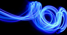 Long Exposure Photograph Of Neon Purple Streaks Of Light In An Abstract Swirl, Parallel Lines Pattern Against A Black Background. Light Painting Photography.