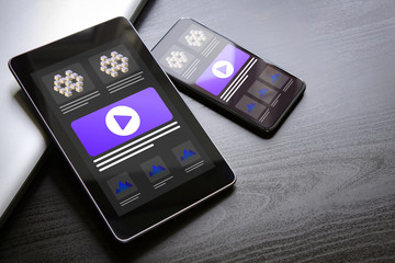 Responsive web site design illustration concept with multiple devices - tablet PC and smart mobile phone lying on a dark wooden table with computer ui ux layout web-design on the screen.