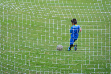 A net of goal  in soccer field with a boy player shooting ball