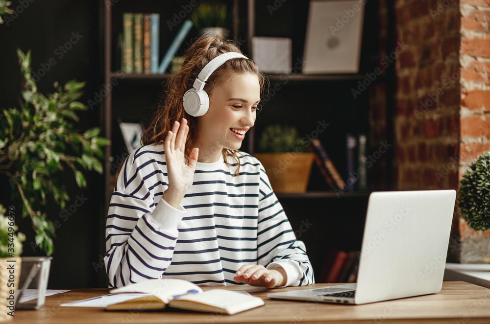 Cheerful woman in headphones greeting friend while talking on laptop at home - obrazy, fototapety, plakaty 