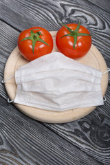 Red tomatoes with green ponytails on a cutting board. Medical mask. On the surface of brushed pine boards.