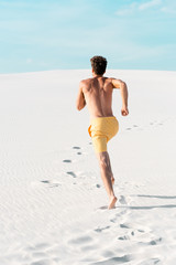 Wall Mural - back view of man in swim shorts with muscular torso running on sandy beach