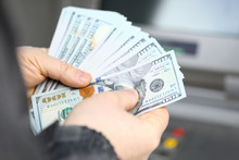 Male Hands Holding Fantail Of Hundred Dollars Banknotes At Atm Machine
