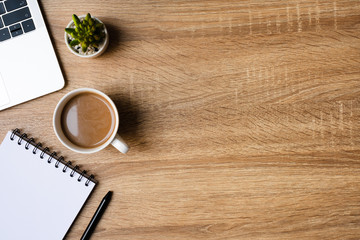 desk office with laptop, blank notepad, coffee cup and pen on wood table. Flat lay top view copy spce.