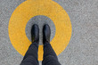 Black shoes standing in yellow circle on the asphalt concrete floor. Comfort zone or frame concept. Feet standing inside comfort zone circle