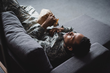 Wall Mural - african american soldier in military uniform holding paper bag while having panic attack and suffering from PTSD at home