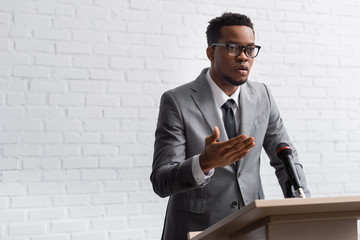 Wall Mural - confident african american business speaker on tribune with microphone in conference hall