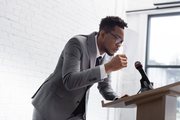 Wall Mural - stressed african american speaker hiding behind paper during business conference