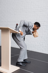 Wall Mural - stressed african american speaker breathing with paper bag and having panic attack on business conference