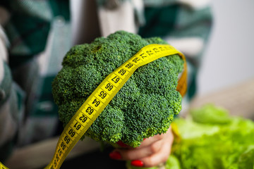 Closeup of woman holding broccoli with string tape to measure