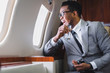 © LIGHTFIELD STUDIOS - stressed african american businessman looking through window while holding pills and glass of water, suffering from panic attack during flight on private plane