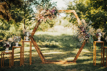 Wedding Wooden Arch In Rustic Style Decorated With Grass Hay Field Color And Flowers. Near Wooden Boxes With Flower Bouquets. Wooden Arch And Flower Decoration. Wedding Ceremony In Sunny Summer Day.