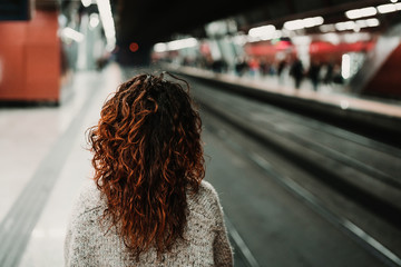 young beautiful woman at train station using mobile phone before catching a train. Back view. Travel, technology and lifestyle concept