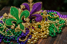 Mardi Gras Color Beads With Fleur De Lis On Wooden Table In Sunlight