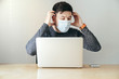 © Mikel Taboada - Man looking away while is putting a mask over his face while is sitting in front of the laptop