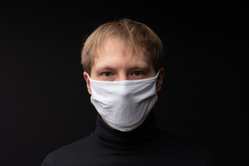 A man in a medical mask looks at the camera. Shot on a black background.