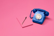 Blue Vintage Antique Rotary Phone On A Pink Background With A Pink Notebook And Pen.  Copy Space And Room For Text With A Right Side Composition.
